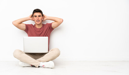 Teenager man sitting on the flor with his laptop frustrated and takes hands on head