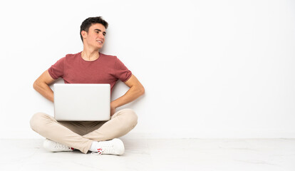 Teenager man sitting on the flor with his laptop suffering from backache for having made an effort