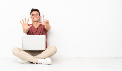 Teenager man sitting on the flor with his laptop counting seven with fingers