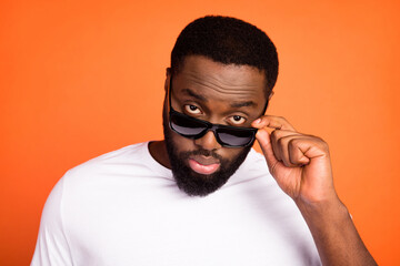 Close-up portrait of attractive dangerous guy wearing touching specs isolated over bright orange color background