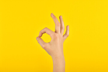 Child's hand showing consent with fingers. Figure on a yellow background. OK.