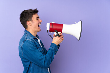 Teenager caucasian  handsome man isolated on purple background shouting through a megaphone