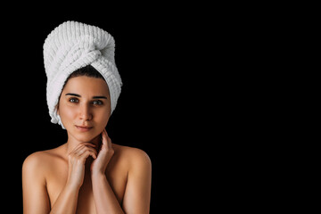 Close-up of a beautiful young woman with a bath towel on her head on a black background. Portrait of a young woman after taking a bath. Sexy girl in a towel on her head. A woman in a spa. Copy space