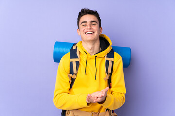 Teenager caucasian mountaineer man with a big backpack isolated on purple background applauding