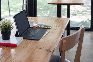 Mockup blank screen tablet with keyboard on wooden table in co-workspace.