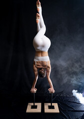 Flexible circus artist - female acrobat doing handstand on the back and smoker background