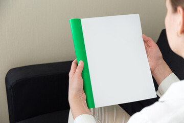 Beautiful female hands hold an open book or magazine in a room on a black sofa