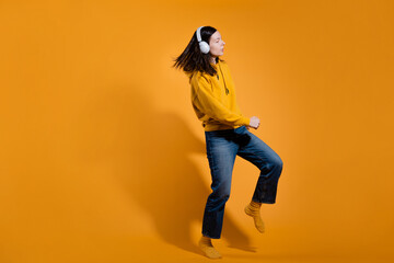 Happy dancing music lover. A young woman in a yellow hoodie with white wireless headphones,