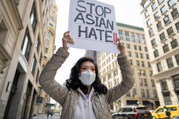 Asian woman holding Stop Asian Hate sign protesting on a street in New York City