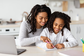 Beautiful black mother helping her daughter with homework - obrazy, fototapety, plakaty