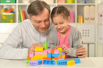 Obraz na płótnie Canvas Father and cute little daughter sitting at table and playing with colorful plastic blocks