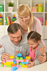Girl with mother and father  playing with colorful plastic blocks