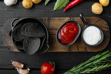 Black crispy potato chips, on black wooden background, top view flat lay