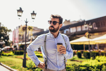 Fototapeta premium Handsome young man in smart casual wear standing on the street while holding coffee cup