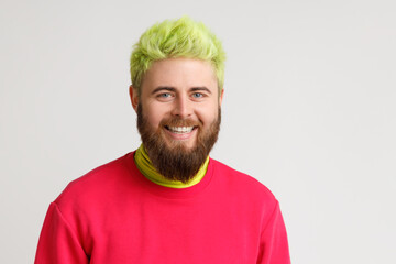 Portrait of handsome Caucasian man with yellow hair and beard, smiles pleasantly, looks directly at camera, being in good mood, wears red jumper. Indoor studio shot isolated on gray background.