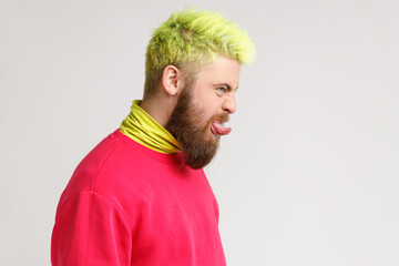 Profile side view of childish carefree man with beard dresses red sweater showing out tongue and...