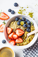 Matcha oatmeal bowl with berries and maple syrup on white marble background, top view. Healthy breakfast, vegan food, detox recipe.