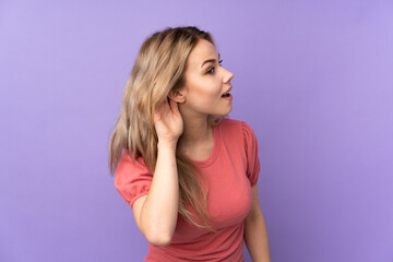 Teenager Russian girl isolated on purple background listening to something by putting hand on the ear