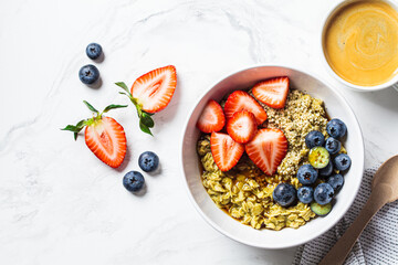 Matcha oatmeal bowl with berries and maple syrup on white marble background, top view. Healthy breakfast, vegan food, detox recipe.