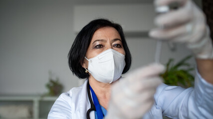 Obraz na płótnie Canvas Portrait of senior woman doctor with syringe standing in hospital, coronavirus concept.