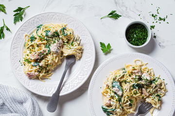 Spaghetti pasta with tuna, spinach and creamy sauce on white plate with fresh herbs, white marble...