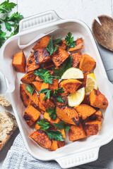 Baked sweet potato wedges with lemon and parsley in baking dish, top view.