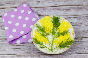 Traditional russian layered salad Mimosa decorated with sprigs of mimosa (made of eggs yolk and dill) on wooden table. Top view