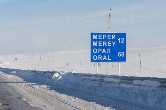 A road sign indicating the settlements of Merey and Oral in the West Kazakhstan region. A winter road cleared of snow.