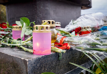 Burning candles and bouquets of flowers on a granite monument. Day of remembrance, sorrow,...