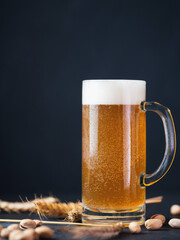 A mug of wheat beer against a black wall. Wheat ears, pistachios copy space
