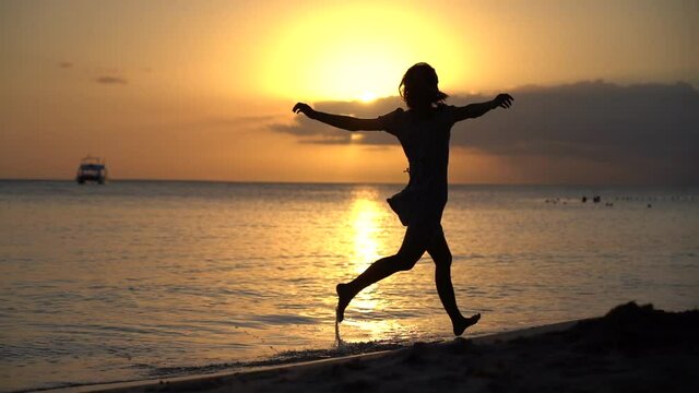 woman in dress running alone on the beach during sunset in slow motion. Concept enjoyment vacation an holiday 