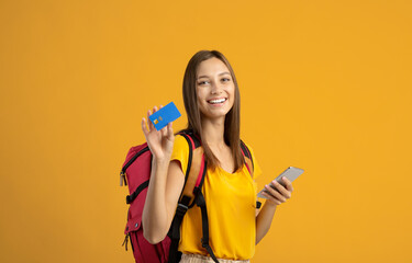 Happy woman backpacker with smartphone and credit card on yellow