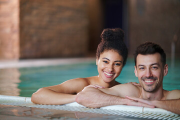 Portrait of young couple in swimming pool, looking at camera.