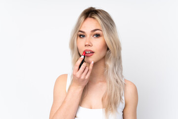 Teenager blonde girl over isolated white background holding red lipstick