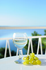Glass of white wine on the table at the balcony with grapes on sea background