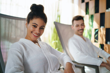 Portrait of young couple sitting and looking at camera in spar resort, relaxing.