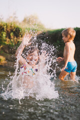 Fototapeta premium Happy summertime, healthy childhood concept. Caucasian children playing, splashing, jumping and having fun in a river in summer. Selective focus on one kid. Vertical shot.
