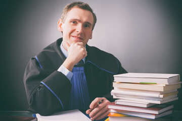 Smiling lawyer in a gown sits at a desk full of books