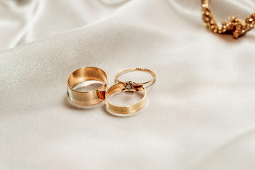 Wedding rings and an engagement ring with diamond on a silk background.