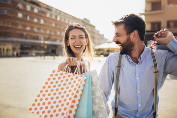 Beautiful couple with shopping bags is talking and smiling while doing shopping in the city