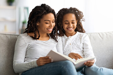 Happy black mother and daughter reading book together