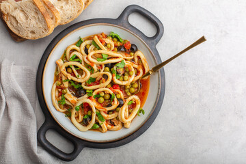 Italian dish - calamari in umido, squid braised in tomatoes, green peas, black olives, garlic,...