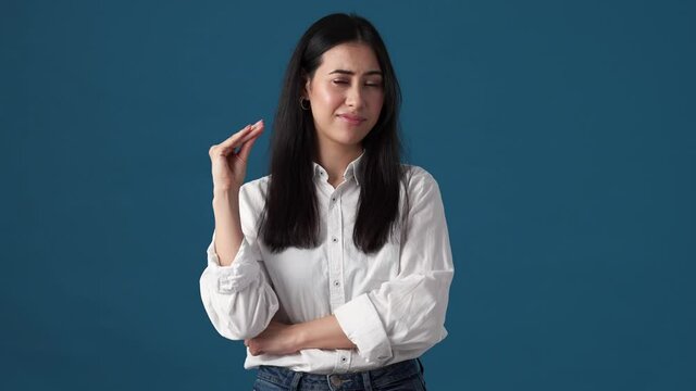 A displeased korean woman is showing stop gesture standing isolated over blue wall in studio