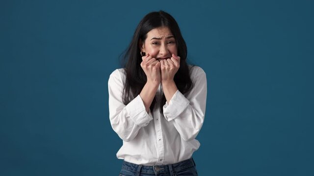 A shocked scared korean woman is opening her mouth while looking to the camera standing isolated over blue wall in studio