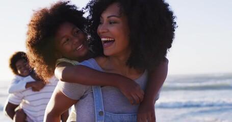 African american mother and father giving a piggyback ride to their daughter and son at the beach - Powered by Adobe