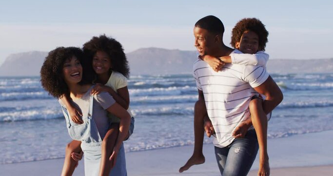 African american mother and father giving a piggyback ride to their daughter and son at the beach