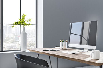 Sunny stylish workspace with city view from big window, plane in white vase and modern monitor on wooden table