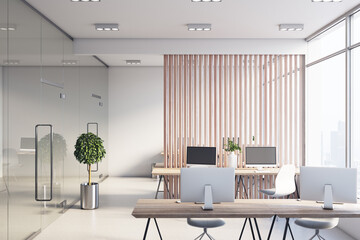 Sunny light spacious office with wooden slatted partition between stylish work places, modern monitors on wooden tables and white floor