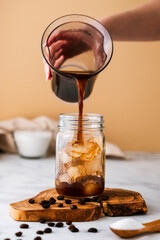 Cold brew coffee being poured over ice. Iced summer drink on light coloured background.
