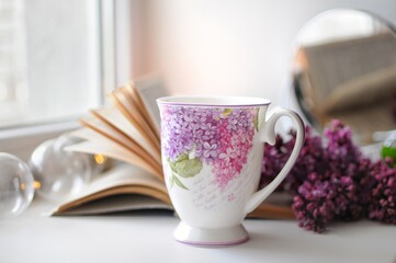 A cup on a white background with lilac bush and a book. Romantic home atmosphere